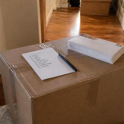 A cardboard moving box on a hallway floor with a checklist, a pen and a stack of envelopes on top