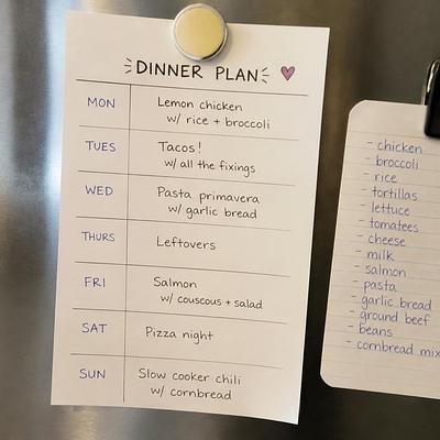 A paper weekly dinner plan stuck to a fridge door, with a short grocery list clipped beside it