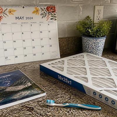 A wall calendar and a notebook on a kitchen counter, with a furnace filter and a toothbrush beside them